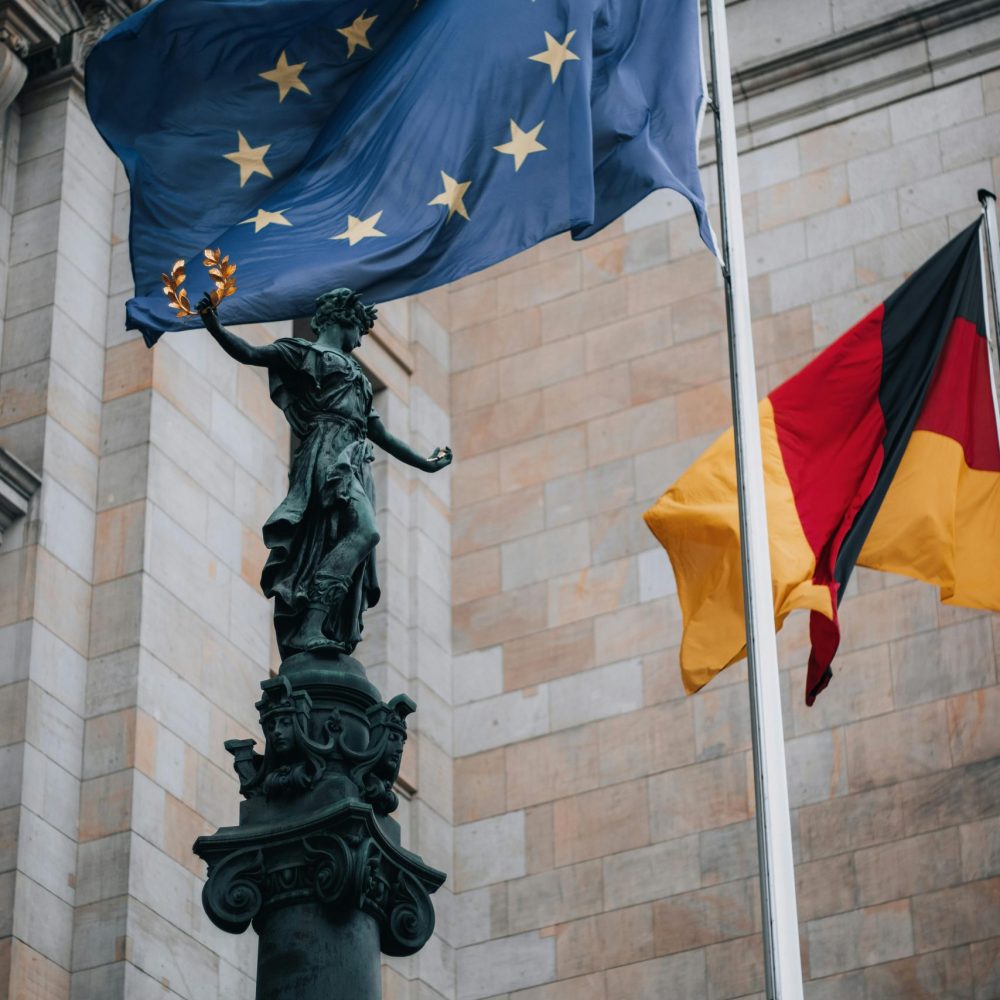 A striking view of the EU and German flags beside a historic sculpture at a landmark building.
