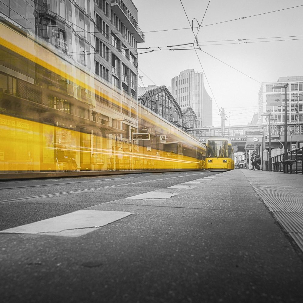Dynamic long exposure of a yellow tram moving through urban streets, showcasing motion blur and city life.